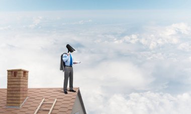 Evin çatısında baş durmak yerine kamerayla zum yapan yüzü olmayan bir iş adamı.