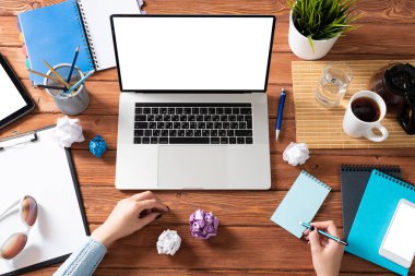 Kadın eli ile modern ofis çalışma alanı. Düz tahta masa, dizüstü bilgisayarlı klavye, bir fincan kahve ve buruşuk kağıt toplarla. İş kadını elleri boş ekranla bilgisayarda çalışıyor.