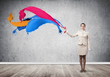 Genç bir kadın kırmızı telefonuyla odada duruyor.