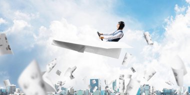 Havacı şapkalı işadamı ve gözlükşehir manzarası üzerinde kağıt uçak sürüyor. Mavi gökyüzünün arka planına bulutlar dökülen kağıtlar. İfade pilotu büyük kağıt uçak eğlenmek.