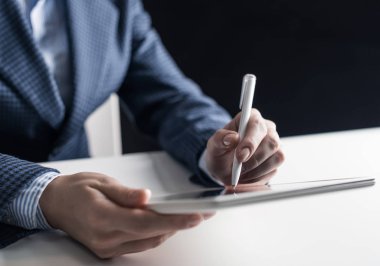 Tablet bilgisayar kullanan takım elbiseli bir adam. Erkek ellerinin kalem ve tablet aletlerini tuttuğu yakın plan. İş yerindeki işadamı. İş hayatı ve hareket kabiliyeti, iş başında internet teknolojisi