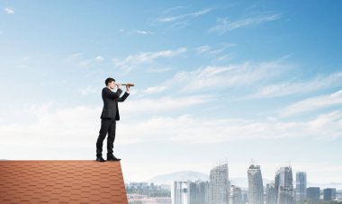 Genç kararlı işadamı çatının tepesinde dikilip dürbüne bakıyor. Karışık ortam