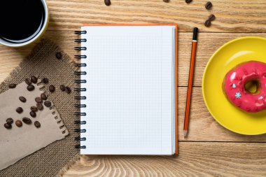 Açılmış not defteri ve bir fincan kahveyle ahşap masada çörek.