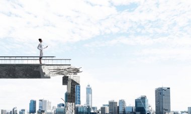 Arka planda Cityscape görünümü ile kırık köprünün sonunda ayakta iken elinde tablet tutan genç ama profesyonel kadın doktor yatay çekim. Medikal Sanayi konsepti