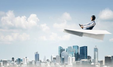 Havacı şapkalı işadamı kağıt düzlemde oturuyor ve direksiyonu tutuyor. Pilot yüksek gökdelenler ve ofis binaları ile iş merkezi üzerinde kağıt uçak sürüş. Bulutlu mavi gökyüzü arka plan