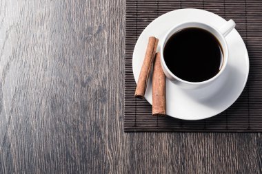 Masada bir fincan sade kahve. Üst görünüm beyaz fincan ve tarçın porselen tabak üzerinde sopalarla. Kafede taze ve aromatik sıcak içecekleri kapatın. Sabah kahvem. Bambu paspas ile Rustik ahşap masa.