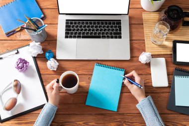 Kadın eli ile modern ofis çalışma alanı. Düz tahta masa, dizüstü bilgisayarlı klavye, bir fincan kahve ve buruşuk kağıt toplarla. İş kadını elleri boş ekranla bilgisayarda çalışıyor.
