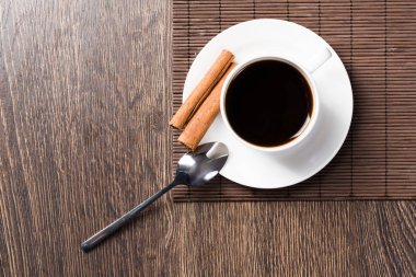 Tahta masada bir fincan espresso kahvesi. Üst manzara beyaz porselen bardak ve çay tabağına tarçın çubukları. Kafedeki taze ve aromatik sıcak içeceği kapat. Sabah kahvesi ve mola zamanı konsepti.