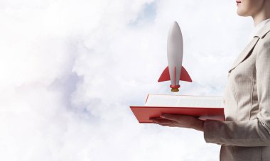 Açık kitapta roket gemisini gösteren kadın. Sembol başlangıç şirketi olarak roket fırlatma. Yeni yaratıcı proje konsepti. Skyscape arka planda beyaz iş elbisesi giymiş kadın. İş inovasyonu.