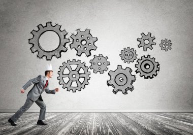 Beyaz kağıt kaplama giyen genç ve yakışıklı işadamı koşuyor ve duvarda dişli mekanizması var.