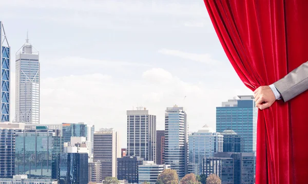 赤いベルベットのカーテンと背景に街並みを開く実業家の手 — ストック写真