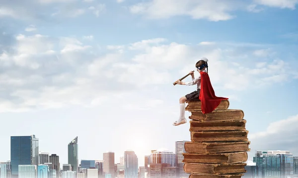 Kleines Kind Maske Und Umhang Schwimmt Auf Bücherstapel Und Schaut — Stockfoto