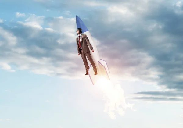 Business person in aviator hat flying on rocket. Progress and innovation technology. Corporate businessman flying with jetpack rocket in blue sky above clouds. Leadership motivation concept.