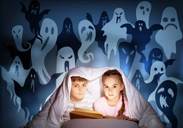 可爱的女孩和男孩在床上读孩子的书 带着手电筒的孩子一起躺在毯子下 穿着睡衣和滑稽鬼的孩子在夜空中剪影 儿童阅读魔法童话 — 图库照片