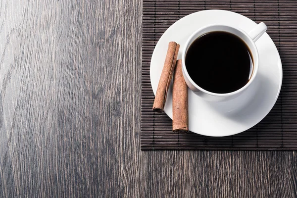 Masada bir fincan sade kahve. Üst görünüm beyaz fincan ve tarçın porselen tabak üzerinde sopalarla. Kafede taze ve aromatik sıcak içecekleri kapatın. Sabah kahvem. Bambu paspas ile Rustik ahşap masa.