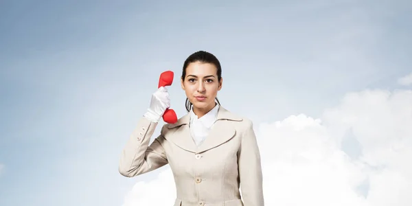 迷人的年轻女人拿着红色的复古电话 穿着白色西装的呼叫中心操作员 在天景背景下摆出电话的姿势 热线电话营销 商业援助和咨询 — 图库照片