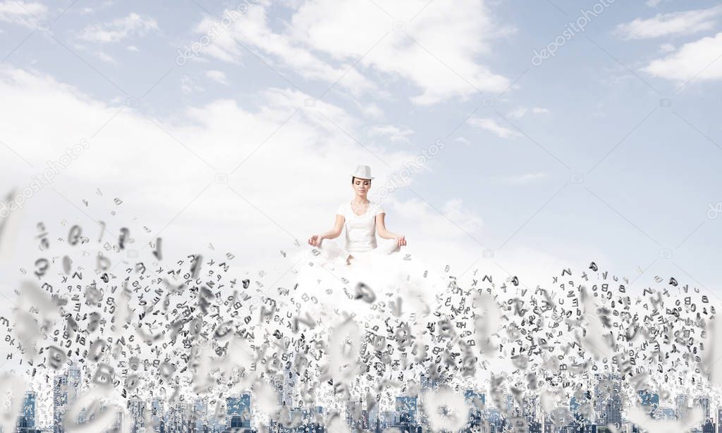 Woman in white clothing keeping eyes closed and looking concentrated while meditating on cloud among flying letters with cityscape view on background.