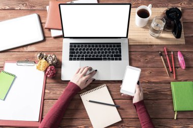 Ofis masasında akıllı telefon kullanan bir iş kadını. Çevrimiçi iş uygulaması kavramı. Kadın eli, dizüstü bilgisayarı ve belgeleri olan düz ofis işyeri. İş için dijital teknoloji ve mobil uygulama.