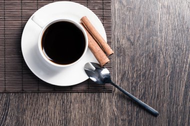 Tahta masada bir fincan espresso kahvesi. Üst manzara beyaz porselen bardak ve çay tabağına tarçın çubukları. Kafedeki taze ve aromatik sıcak içeceği kapat. Sabah kahvesi ve mola zamanı konsepti.