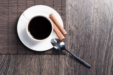 Tahta masada bir fincan espresso kahvesi. Üst manzara beyaz porselen bardak ve çay tabağına tarçın çubukları. Kafedeki taze ve aromatik sıcak içeceği kapat. Sabah kahvesi ve mola zamanı konsepti.