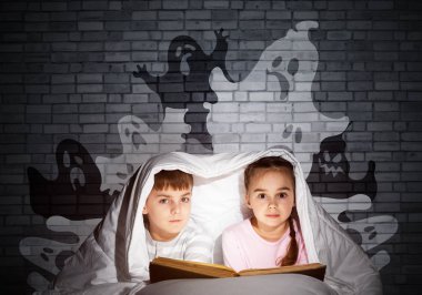 Sevimli kız ve erkek yatakta çocuk kitap okuma. El feneri olan çocuklar battaniyenin altında yatıyorlar. Pijamalı çocuklar ve komik hayaletler gri duvara geri siluetler. Sihirli peri masalları okuyan çocuklar