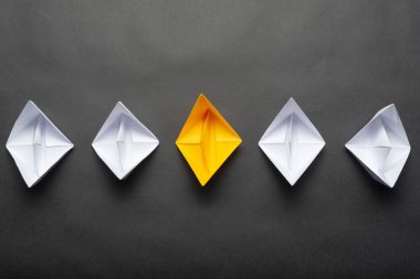 Siyah arka plan üzerinde kağıt gemi sırası. Yaratıcı yenilik ve liderlik iş kavramı. Düz beyaz tekne grubunda sarı origami tekne yatıyordu. Kopyalama alanı ile sosyal pazarlama düzeni.
