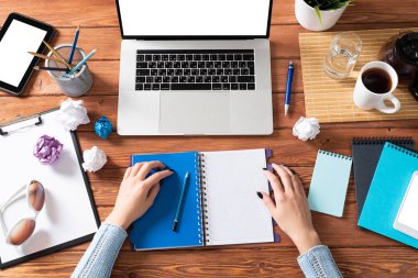 Ofis masasındaki not defterine yazan iş kadını. Çevrimiçi iş öğrenimi ve eğitim. Kadın eli, dizüstü bilgisayarı ve belgeleri olan düz ofis işyeri. Dijital teknoloji ve ortak çalışma alanı