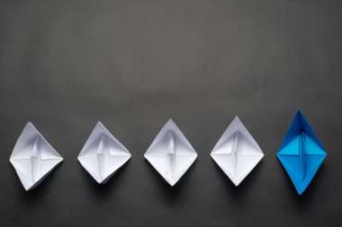 Siyah arka planda kağıt gemiler. Beyazlar arasında öncülük eden mavi kağıt gemiyle liderlik kavramı. Bireysel motivasyon ve yön. Kopya alanı olan sosyal pazarlama düzeni.