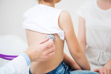 Pediyatrist steteskopla küçük çocuğu muayene ediyor. Küçük kızın tıbbi muayenesi. Profesyonel klinik teşhisler. Steteskoplu doktor eli. Anne ve kızı klinikte.