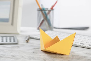 Sarı kağıt gemi ile modern ofis çalışma alanı. Bilgisayar klavyesi, hesap makinesi ve belgeler ile düz yatıyordu ahşap masa. Yaratıcı pazarlama ve reklam ajansı. İşadamı liderliği ve yönü