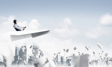 Havacı mavi gökyüzünde iş merkezi üzerinde kağıt uçak sürüş. İş belgeleriyle çalışmak. Gökdelenlerin arka planına düşen kağıtlar. Deri kasklı pilot kağıt düzlemde oturuyor