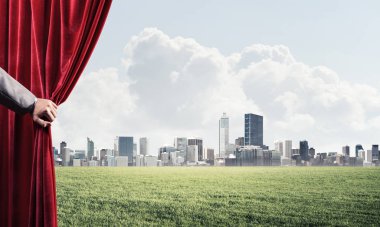İnsan eli kırmızı kadife perde cityscape ve yeşil çayır açar