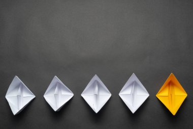 Siyah arka plan üzerinde kağıt gemi sırası. Yaratıcı yenilik ve liderlik iş kavramı. Düz beyaz tekne grubunda sarı origami tekne yatıyordu. Kopyalama alanı ile sosyal pazarlama düzeni.