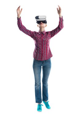 Gri arka plana karşı sanal gerçeklik gözlüğü takan genç kadın. Elleri havada damalı gömlek li ve kot pantolonlu güzel kadın. Dijital arayüzle etkileşim. Geleceğin teknoloji konsepti