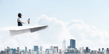 Kağıt uçakta oturan pilot ile iş motivasyonu kavramı. Havacı şapkalı komik adam ve şehrin üzerinde kağıt uçak süren gözlükler. Rüyada gökyüzünde uçmak. Yüksek binalarile modern megapolis.