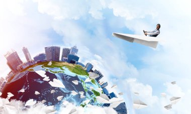 Havacı şapkalı işadamı kağıt düzlemde oturuyor ve direksiyonu tutuyor. Bulutlu mavi gökyüzünde kağıt uçak kullanan pilot. Yüksek gökdelenler ve deniz hattı ile modern şehrin küresel görünümü.