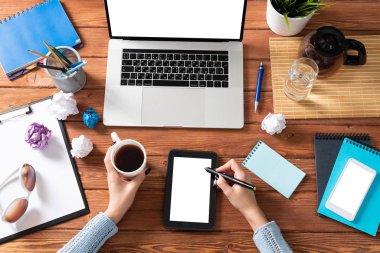 Ofis masasında çalışan bir iş kadını. Düz tahta masa, dizüstü bilgisayarı ve beyaz ekranlı tablet bilgisayarı vardı. Kadın eli ile üst düzey ofis işyeri. Çevrimiçi iş ve internet ticareti