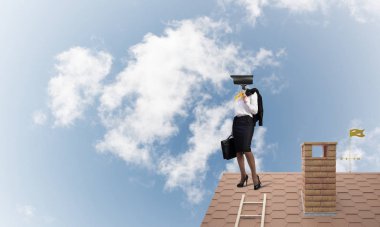 Evin çatısında baş durmak yerine kamerayla zum yapan yüzsüz iş kadını.