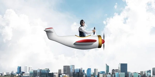 Businessman in aviator hat and goggles driving propeller plane above downtown with high modern buildings. Successful leader flying in small airplane. Blue sky landscape with clouds on background