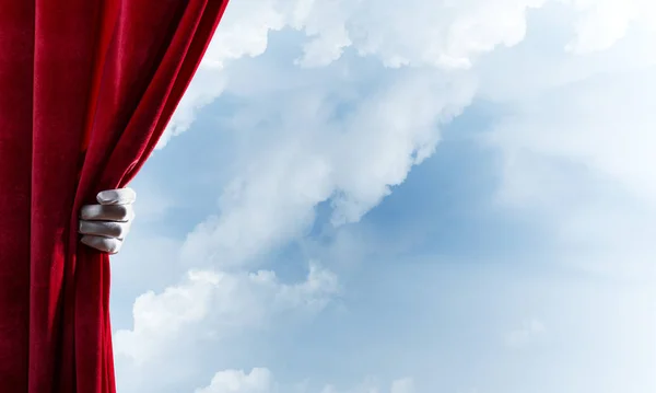 手袋で人間の手が開き青い空を背景に赤いベルベットのカーテン — ストック写真