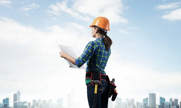 戴着硬礼帽的女工程师站在技术蓝图旁边 城市景观背景下穿着格式化蓝色衬衫的女建筑师侧观 建筑项目管理 — 图库照片