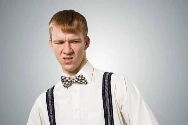 多么恶心 不高兴的红头发嬉皮士 喜怒无常的男孩看到令人厌恶或厌恶的事情时 脸上都会流露出不满意的表情 穿着白衬衫 领结和吊带衫的人的画像 — 图库照片