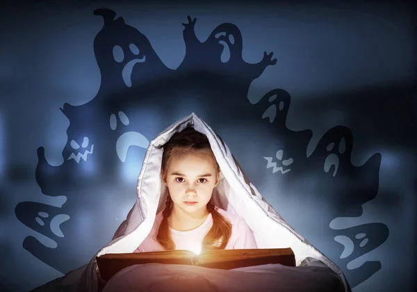 Scared kid with reading book under blanket — 스톡 사진