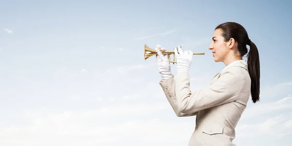 Business woman playing trumpet brass. Young lady in white business suit and gloves posing with music instrument on blue sky background. Business assistance and support concept with musician.