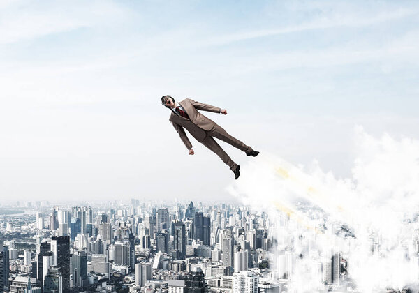 Businessman in suit and aviator hat flying in blue sky as superhero. Business person as superman with jet flame above modern downtown. New challenges and winning. Career ambition and growth