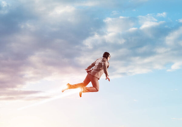 Businessman in suit and aviator hat flying in blue sky as superhero. Corporate manager as superman launching upwards with jet flame in stratosphere. Successful business startup motivation concept