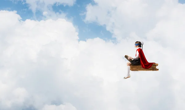 空に本の上に浮かぶマスクとケープの小さな子供と読書 — ストック写真