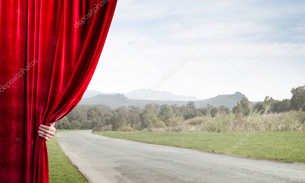 Human hand opens red velvet curtain to landscape with road