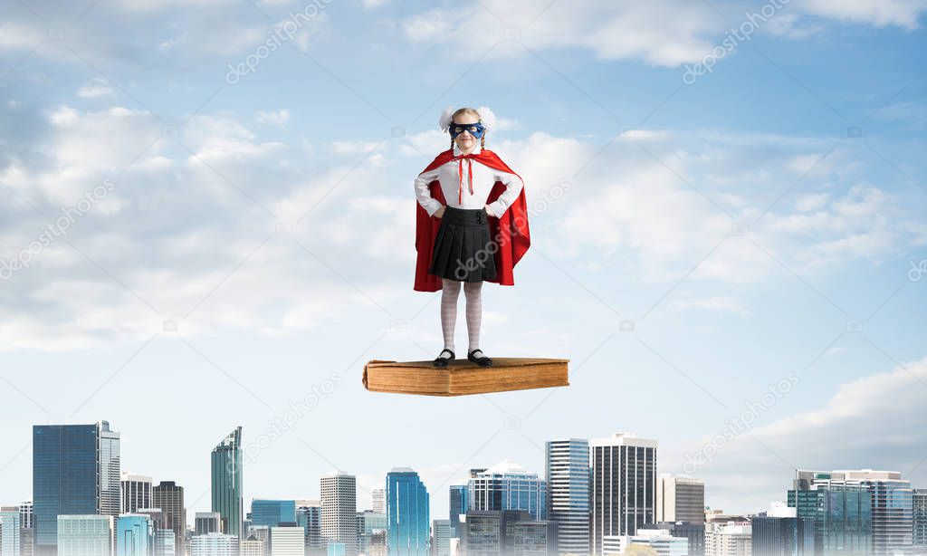 Young girl in superhero costume standing on old floating book. Mixed media