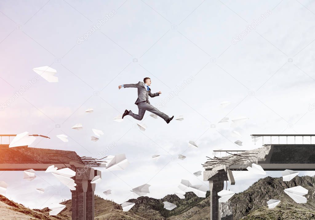 Businessman jumping over gap in bridge among flying paper planes as symbol of overcoming challenges. Skyscape with sunlight and nature view on background. 3D rendering.